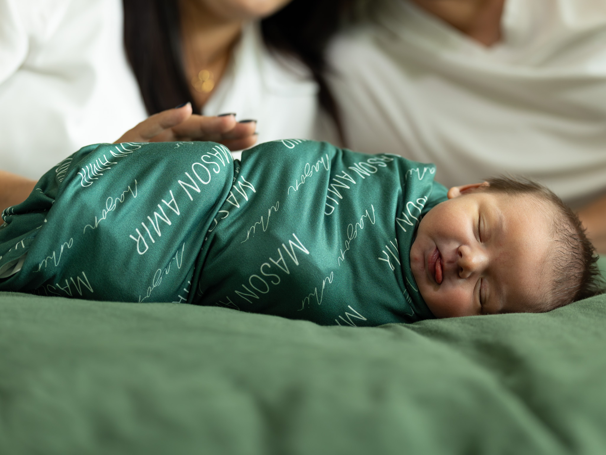 Newborn wrapped in a soft green blanket with a playful tongue out expression